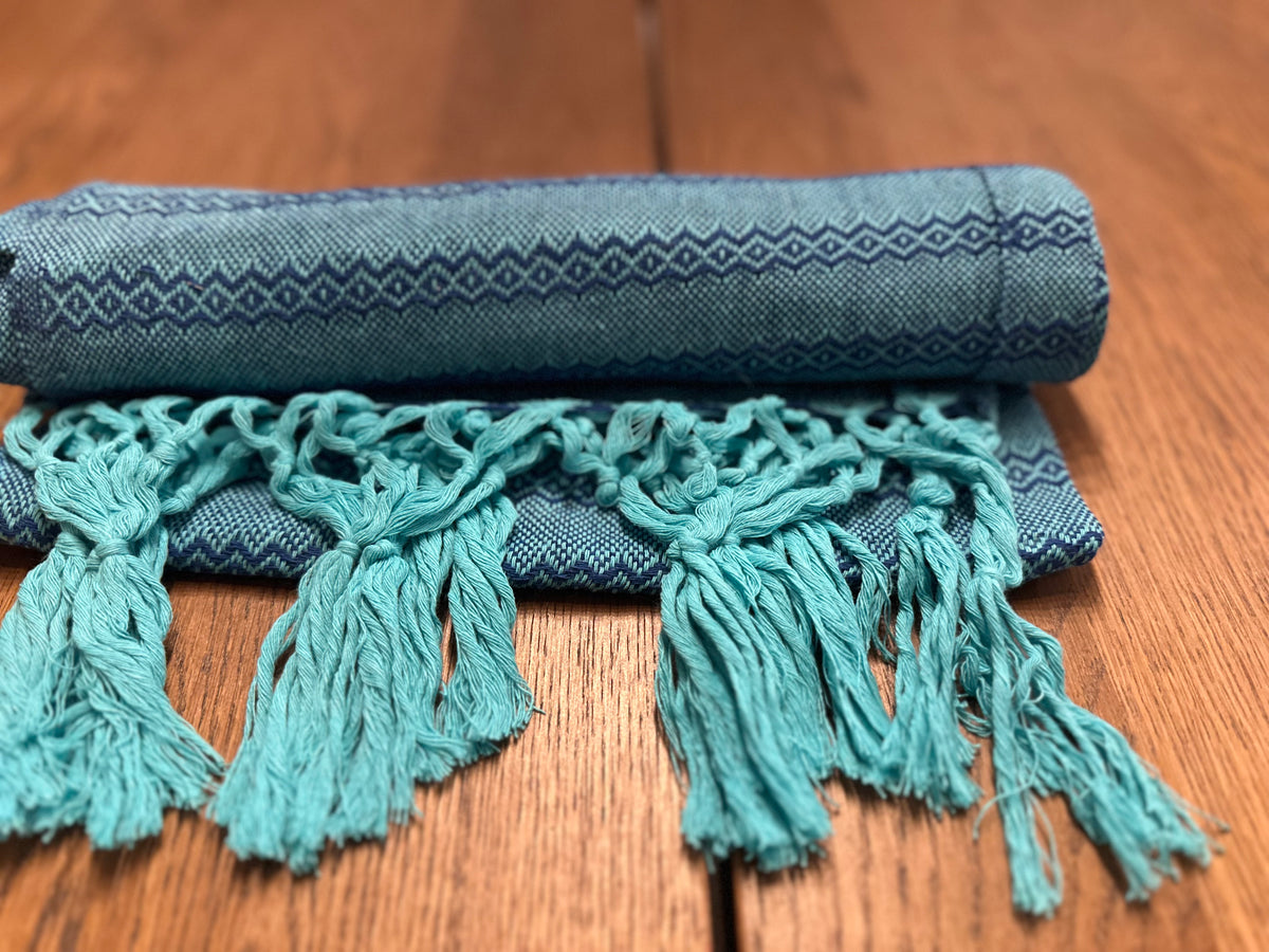 Agua de Mar turquoise and navy Mexican rebozo baby wrap rolled with turquoise hand-knotted fringe in front | Lola My Love