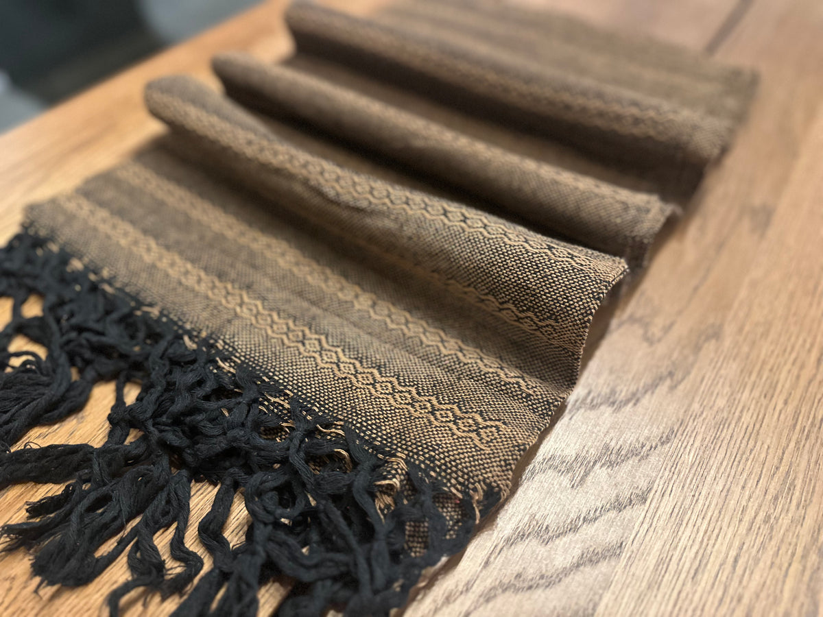 Noche de Mezcal Mexican rebozo baby wrap in soft folds showing the black hand-knotted fringe and tan zigzag weave | Lola My Love